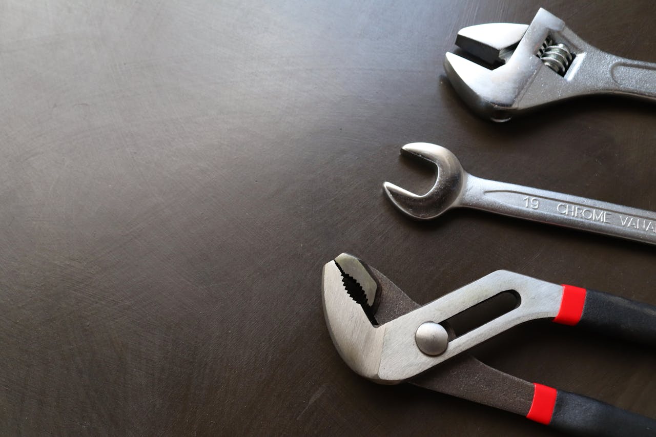 about-01 High-quality image of various metal tools including wrenches and pliers arranged on a dark surface.
